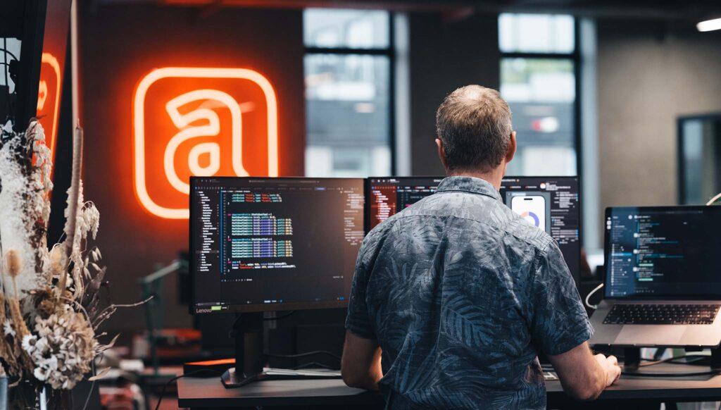 man working on desk with 3 screens